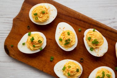 Beyaz ahşap arka planda, ahşap bir tahtanın üzerinde soğanlı ev yapımı Deviled Eggs, üst manzara. Dümdüz, tepeden, yukarıdan. 