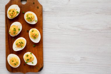 Beyaz ahşap bir yüzey üzerinde ahşap bir tahtanın üzerinde soğanlı ev yapımı Deviled Eggs, üst manzara. Dümdüz, tepeden, yukarıdan. Boşluğu kopyala.