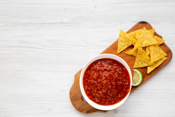 Homemade Tomato Salsa and Nachos on a rustic wooden board on a white wooden table, top view. Flat lay, overhead, from above. Copy space.