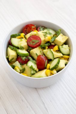 Taze Avokado Domates Salatası beyaz ahşap arka planda bir kasede, yan görünüm. 