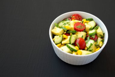 Taze Avokado Domates Salatası, siyah bir yüzey üzerinde bir kasede, yan görünüşte. Metin için boşluk.