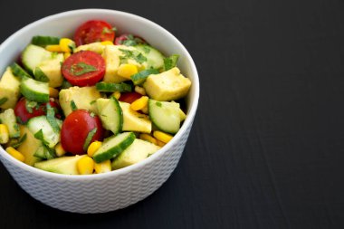 Taze Avokado Domates Salatası, siyah bir yüzey üzerinde bir kasede, yan görünüşte. Boşluğu kopyala.