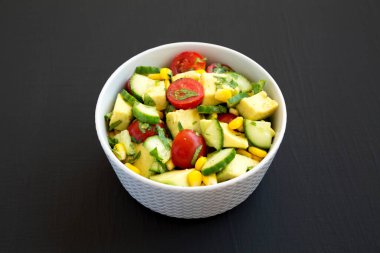 Taze Avokado Domates Salatası siyah arka planda bir kasede, yan görünüm.
