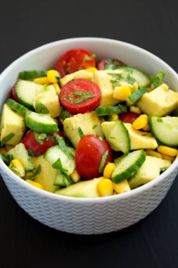 Siyah arka planda bir kasede taze Avocado Domates Salatası, yan görüş. Yakın plan..