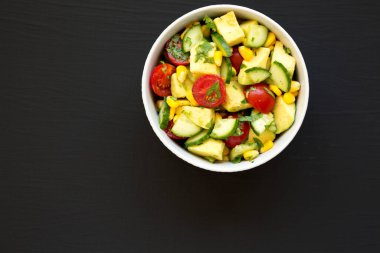 Taze Avokado Domates Salatası, siyah bir yüzey üzerinde bir kasede, üst manzara. Dümdüz, tepeden, yukarıdan. Boşluğu kopyala.