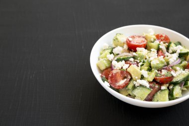 Lezzetli Avokado Domates ve salatalık salatası siyah bir yüzey üzerinde beyaz bir kasede, yan görünüşte. Boşluğu kopyala.