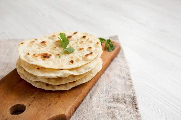 Ev yapımı Roti Chapati yassı ekmeği beyaz ahşap bir yüzey üzerinde ahşap bir tahta üzerinde yan görüş. Boşluğu kopyala.