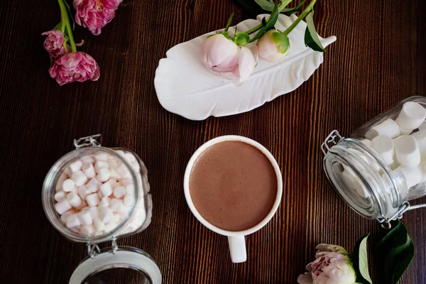 Cocoa with marshmallow and flowers on table.