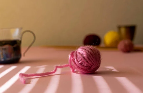 Pembe yün yumağı ve sabah güneşinin gölgeleri. Çay fincanı, ahşap örgü iğneleri ve bulanık arka planda yün toplar. Kopya için yer. 