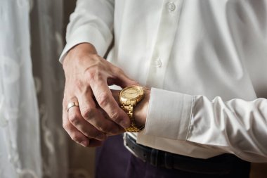 İş adamı kol saatini kontrol ediyor, saati eline alıyor, damat düğün töreninden önce hazırlanıyor.