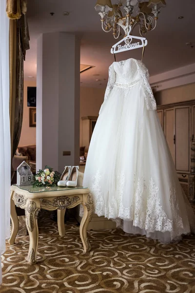 beautiful wedding dress hanging in the room, woman getting ready before  ceremony