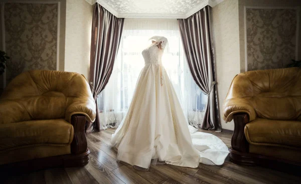 beautiful wedding dress hanging in the room, woman getting ready before  ceremony