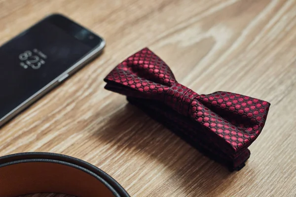 Different men's accessories such as: belt, bow tie and telephone - are on the table