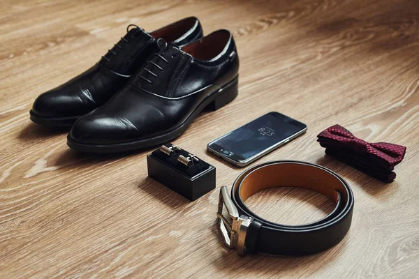 Different men's accessories such as: shoes, belt, bow tie, cufflinks and telephone - are on the table