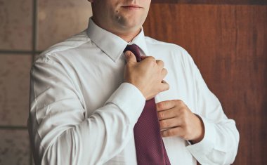 Gömlekli bir adam evde kravat takıyor.