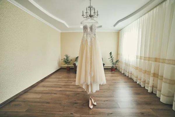 beautiful wedding dress hanging in the room, woman getting ready before  ceremony