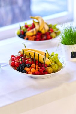 Plaka ile lezzetli meyve muz, çilek, üzüm, şeftali ve armut gibi. Vejetaryen yiyecekler. Masanın üzerine karışık meyveli kase