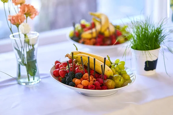 Plaka ile lezzetli meyve muz, çilek, üzüm, şeftali ve armut gibi. Vejetaryen yiyecekler. Masanın üzerine karışık meyveli kase
