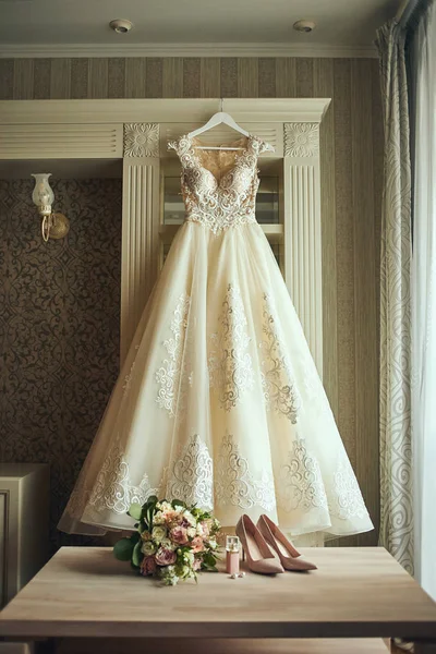 beautiful wedding dress hanging in the room, woman getting ready before  ceremony