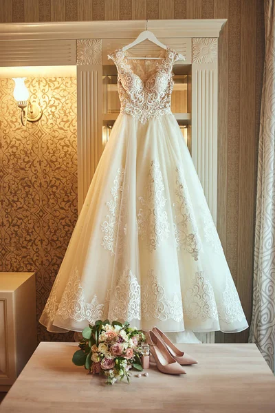 beautiful wedding dress hanging in the room, woman getting ready before  ceremony