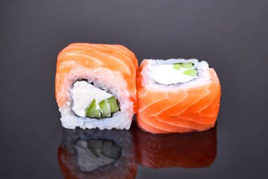 Menü için siyah arka plan üzerinde somon, avokado ve krem peynir ile Philadelphia rulo suşi. Japon yemekleri