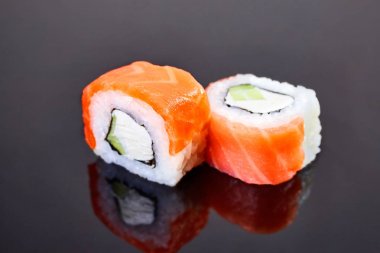 Menü için siyah arka plan üzerinde somon, avokado ve krem peynir ile Philadelphia rulo suşi. Japon yemekleri
