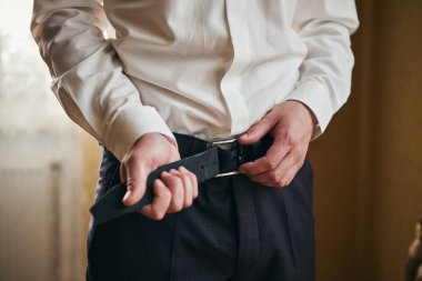 İş adamı kemer takıyor, moda ve giysi konsepti, damat törenden önce sabah hazırlanıyor.