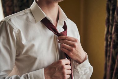 Gömlekli bir adam evde kravat takıyor.