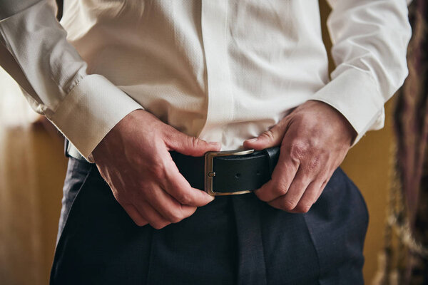 Businessman putting on a belt, fashion and clothing concept,groom getting ready in the morning before ceremony