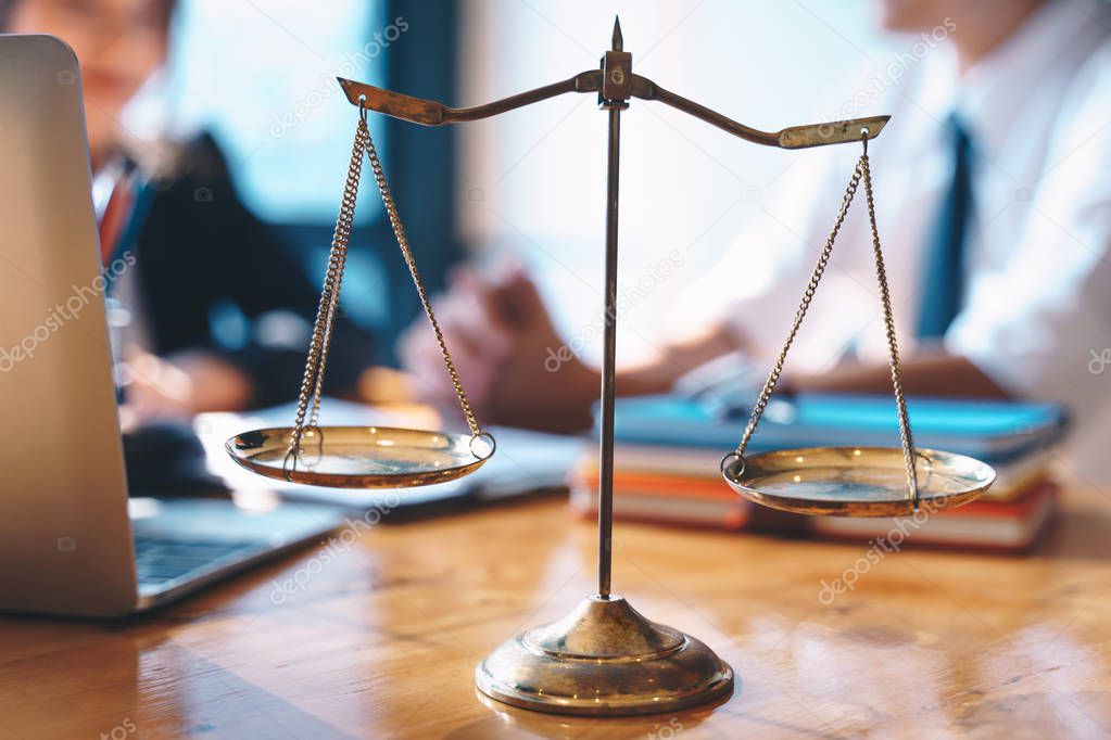 Scales of justice on wooden table background with Businesswoman and male lawyers discussing contract papers at the law firms. Legal law, lawyer, advice and justice concept.
