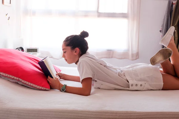 A jovem rapariga está a ler um livro na cama dela. — Fotografia de Stock