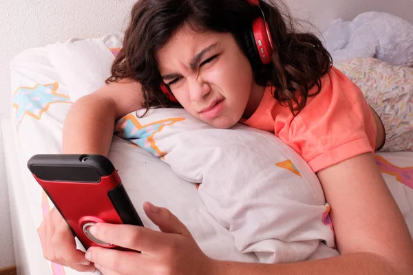 Remaja mendengarkan musik dari ponselnya dengan headphone di tempat tidurnya — Stok Foto