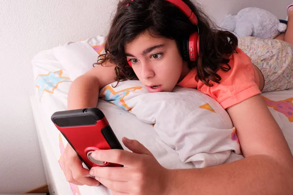 Remaja mendengarkan musik dari ponselnya dengan headphone di tempat tidurnya — Stok Foto