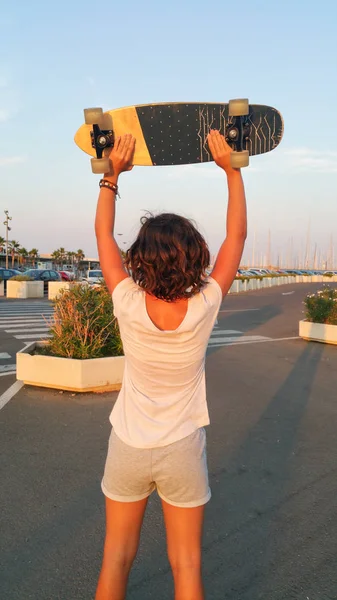 Adolescente em suas costas levantando um skate ao pôr do sol — Fotografia de Stock