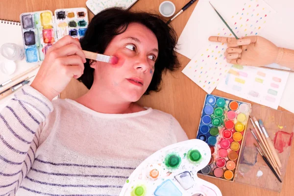 woman painting her face with watercolors and watercolor utensils around
