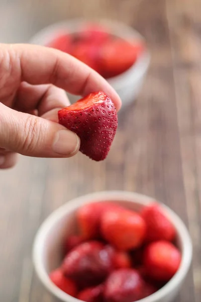 Man's hand picking strawberry from a bowl of strawberries on wooden background — Stock Photo, Image