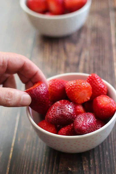 Man's hand picking a strawberry from a bowl of strawberries on wooden background — Stock Photo, Image