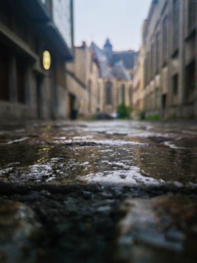 Arka planda Ghent şehrinin odaksız panoramik manzarası ile ıslak sokakların altından görünümü