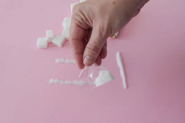 Mano de una mujer con un paquete de azúcar como si fuera droga sobre fondo rosa —  Fotos de Stock