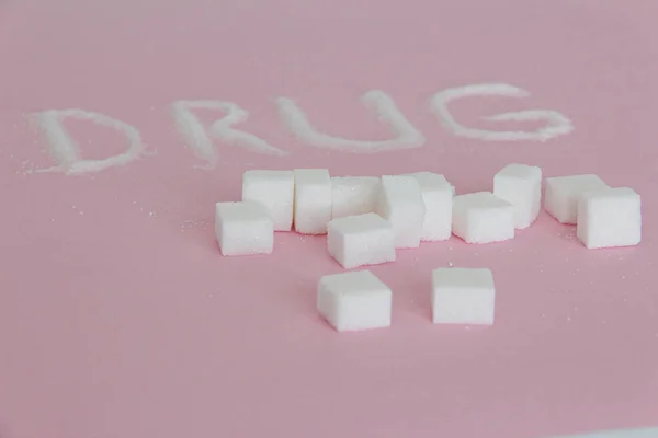 Слово Наркотики, написані кубиками цукру на рожевому фоні — стокове фото