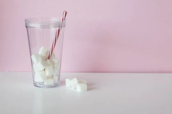 Cubos de azúcar blanco dentro de un vaso con una paja sobre fondo rosa y blanco Imágenes De Stock Sin Royalties Gratis