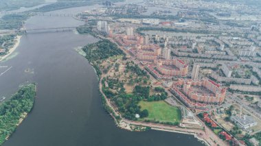 Nehir kıyısında üzerinde kırmızı binaların havadan görünümü. Bir park. Köprü.