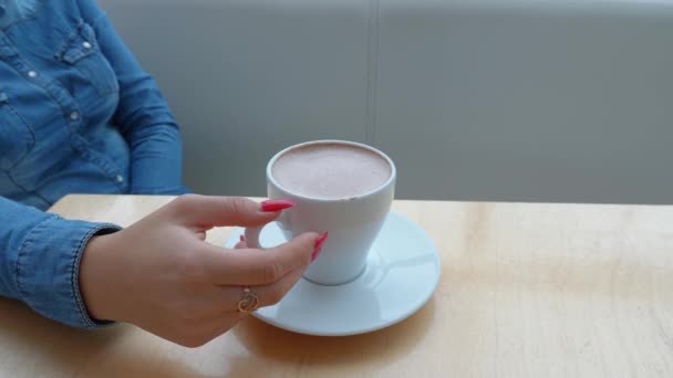 青いデニムのシャツを着た女の子がカフェでコーヒーの白いカップを保持しています — ストック動画