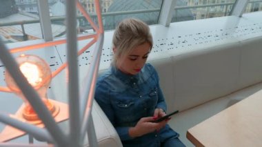 Kız bir kafede bir akıllı telefon görünüyor. Telefonda bir iletiyi arar.