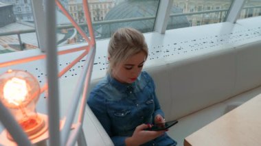 Kız bir kafede bir akıllı telefon görünüyor. Telefonda bir iletiyi arar.