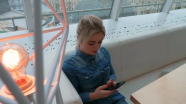 Kız bir kafede bir akıllı telefon görünüyor. Telefonda bir iletiyi arar.