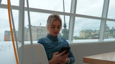 Kız bir kafede bir akıllı telefon görünüyor. Belgili tanımlık smartphone üzerinde çalışmak.