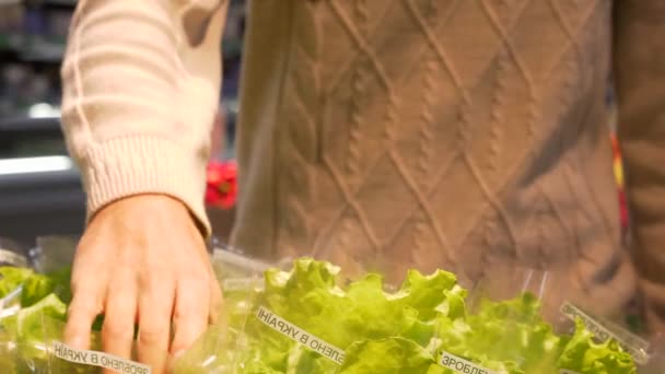 若い男はレタスを手に取るし 葉します スーパー マーケットでカウンターからパッケージのレタス グリーンを取ります 健康食品 — ストック動画