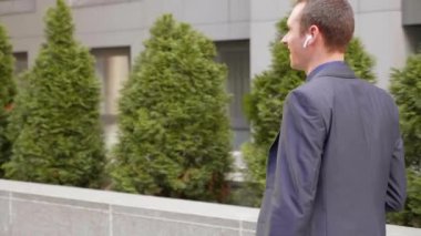 Kablosuz kulaklıkla yürüyen ve mutlu bir telefon görüşmesi yle iletişim kuranan genç bir işadamı. Elinde bir bardak kahve ile neşeli bir adam konuşurken gülümsüyor. 4k görüntü.