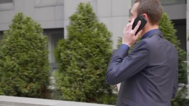 Genç bir işadamı sokakta yürüyor ve telefon görüşmesi hakkında konuşuyor. Elinde bir bardak kahve ile klasik takım elbiseli bir adam akıllı telefonda bir konuşma yol açar. 4k görüntü.